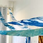 a pulled back view of four, narrow cyanotype banners running across a ceiling. Each is a different shade of blue